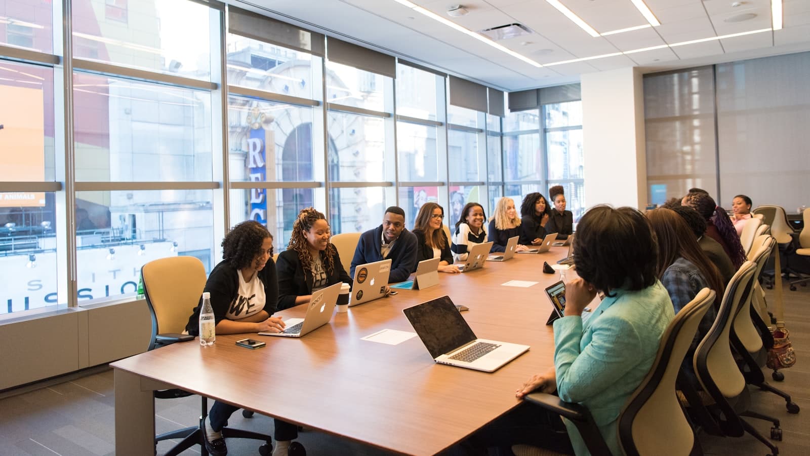 A group of colleagues sitting around a long boardroom table with laptops open, in discussion